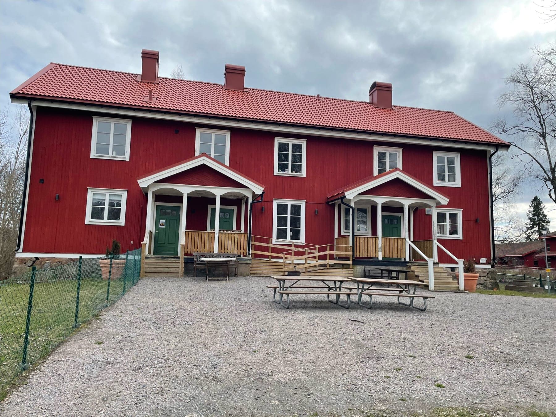 Ett av Fröstugans faluröda hus, med vita knutar, gröna dörrar och picknickbord på grusplanen framför.
