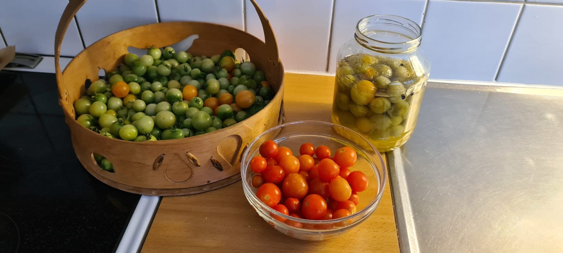 Nyskördade tomater i en korg och en glasburk med inlagda gröna tomater på köksbänken.